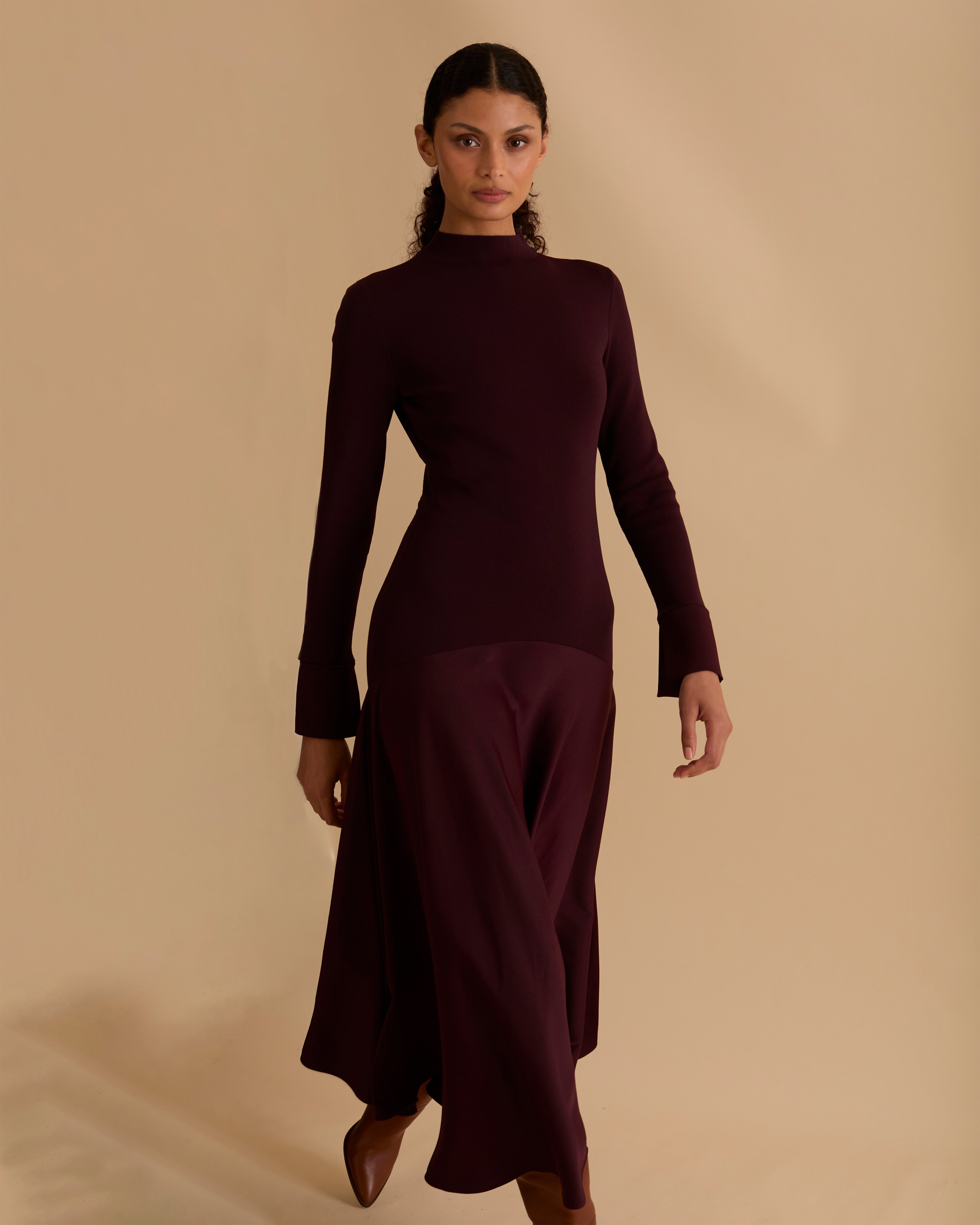 Model wearing Florere iconic signature Acacia dress. Knitted fabric for a fitted bodice, with dropped waist satin midi skirt with dramatic flare. Wearing tan knee high boots, against a beige neutral backdrop