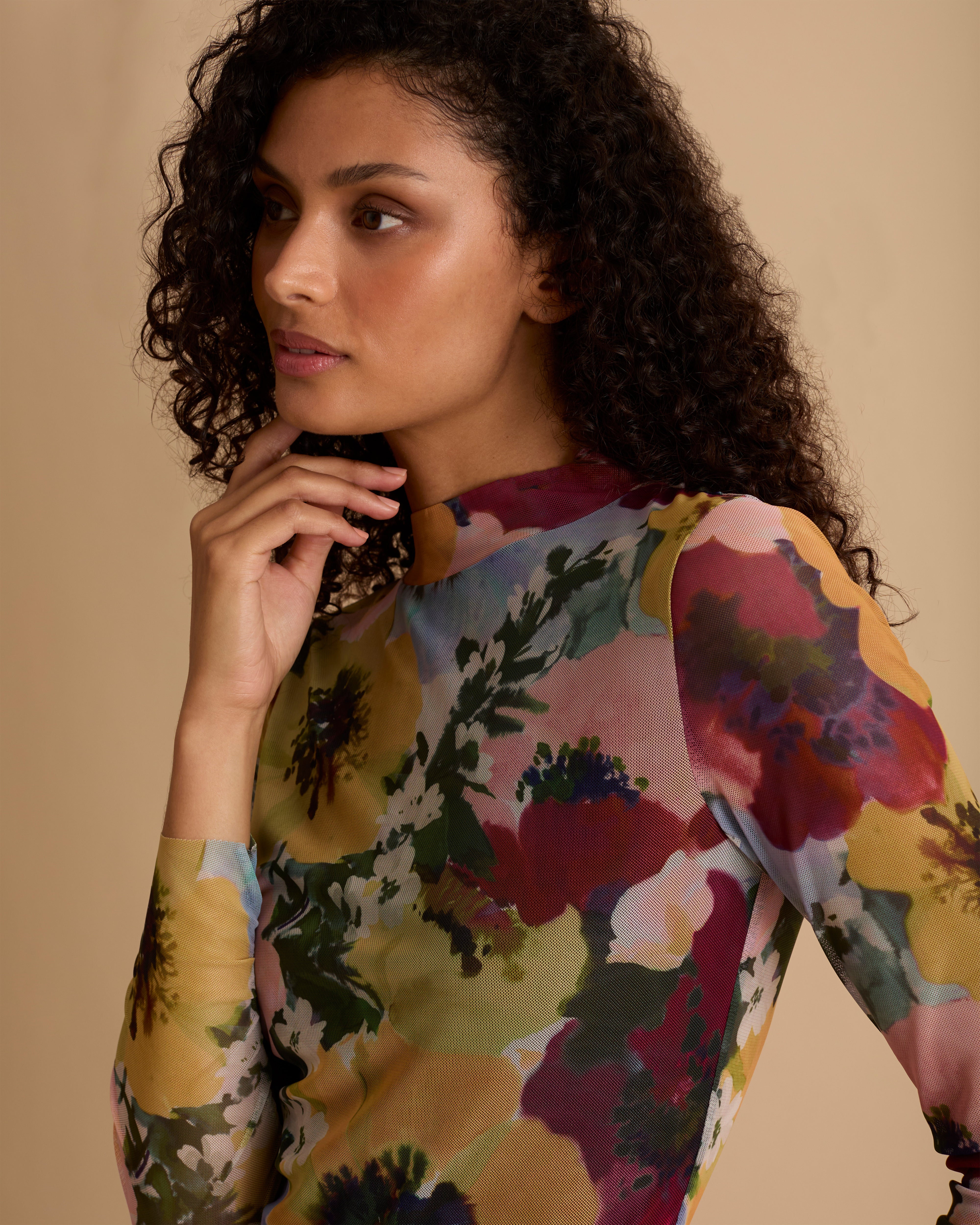 Model wearing Florere floral print mesh top with high neck and long fitted sleeves. Wearing with Florere wide leg pleated burgundy trousers against a neutral back drop