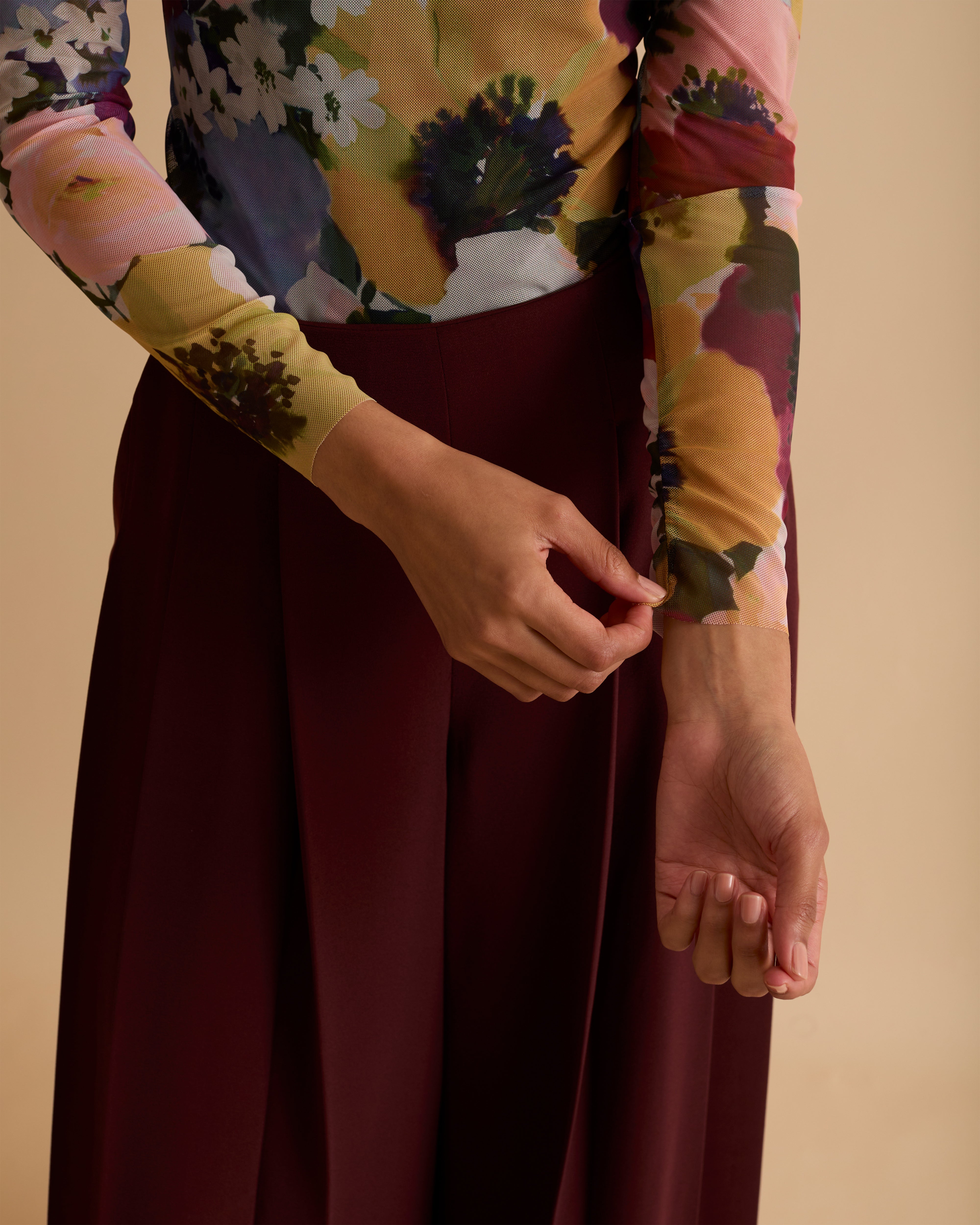 Model wearing Florere floral print mesh top with high neck and long fitted sleeves. Wearing with Florere wide leg pleated burgundy trousers against a neutral back drop